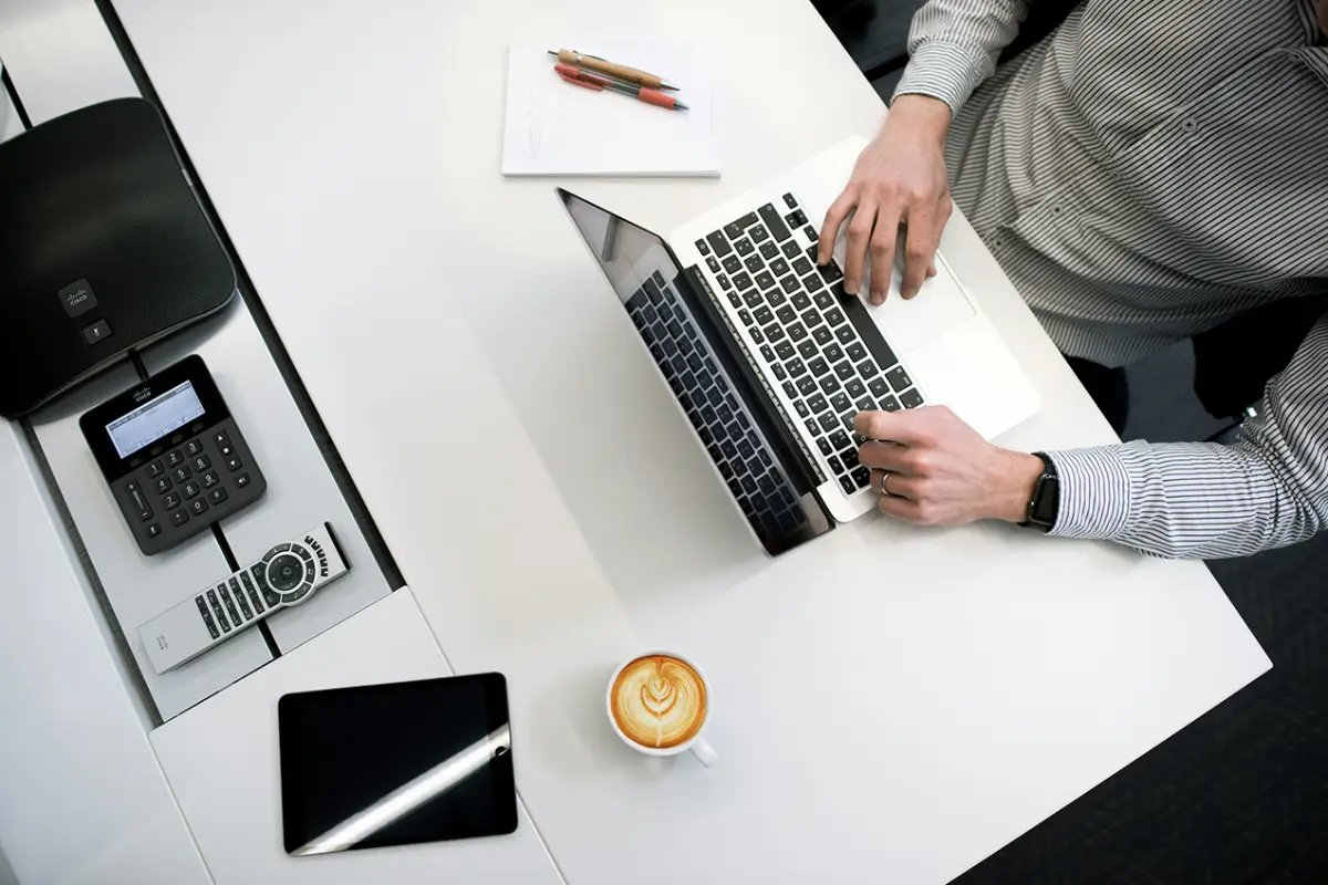 Worker on a laptop with various other items on top of a desk.
