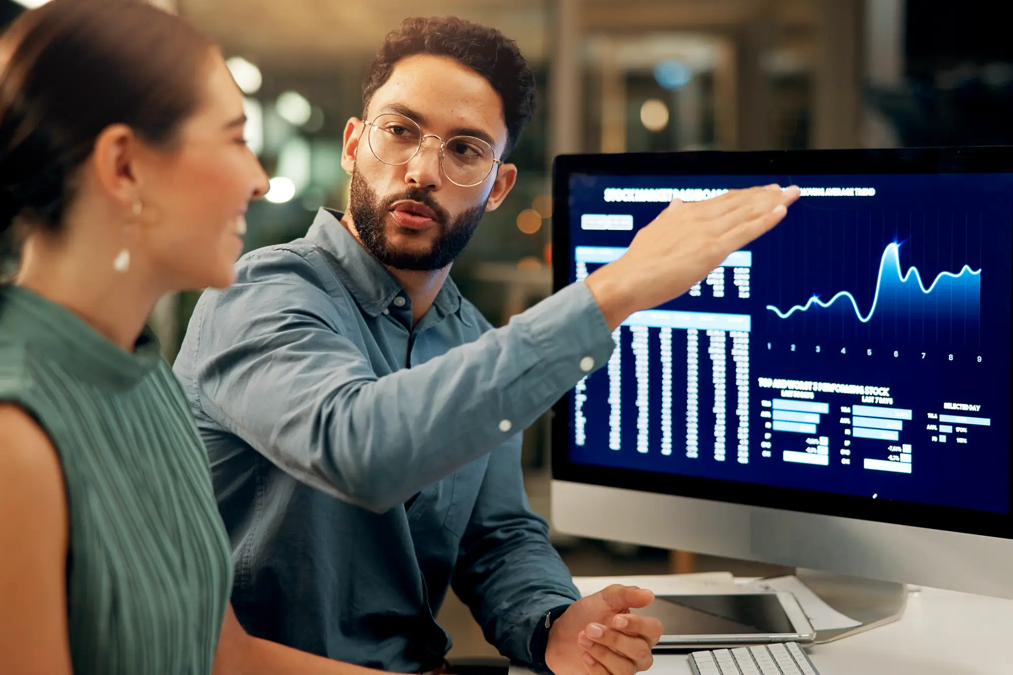 Man with glasses holding his arm in an upwards slant while discussing data with a colleague. 