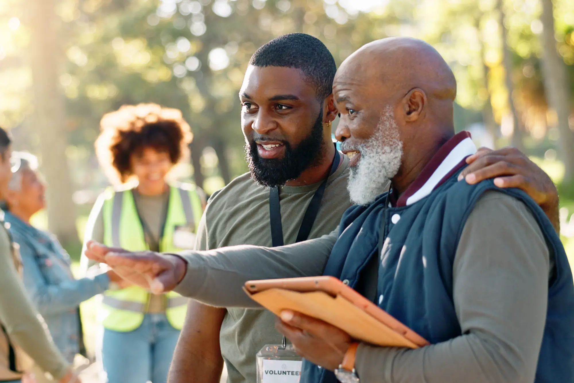 An older man with a clipboard and middle-aged man talking during a volunteer event.