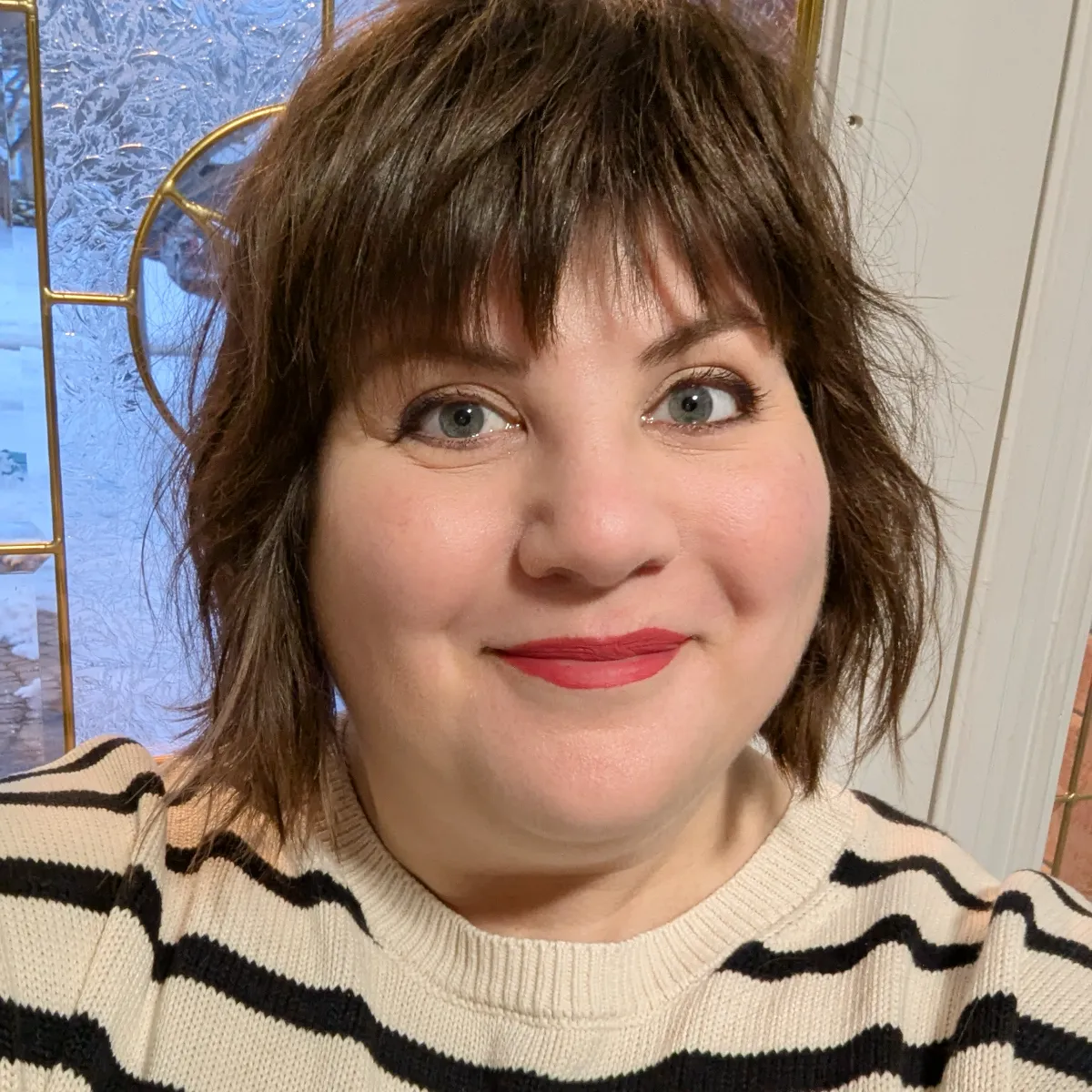 A headshot of Laura Gale, who has short brown hair and light eyes, smiling warmly while wearing a black and cream striped sweater.
